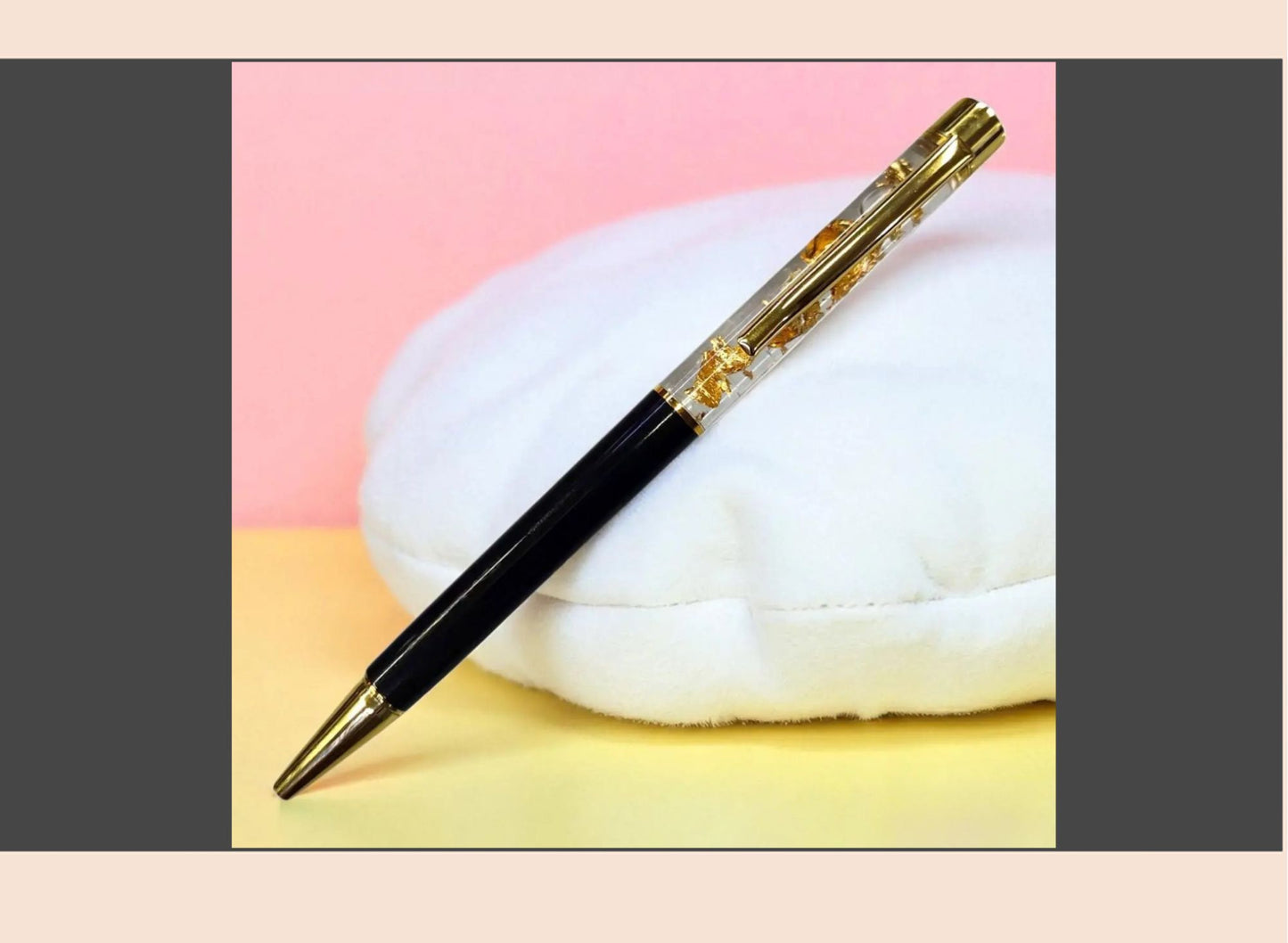 Pen with black and gold accents on a white cloud-like object against a pink and yellow background