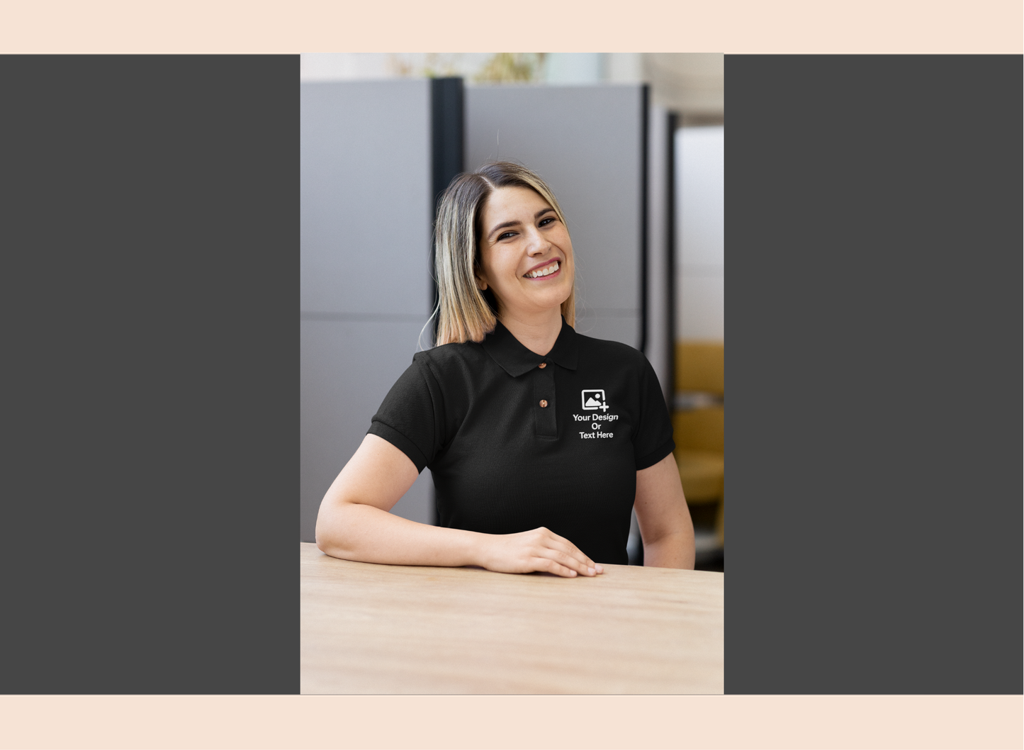 Woman wearing a black polo shirt with a logo, sitting at a desk in an office setting.