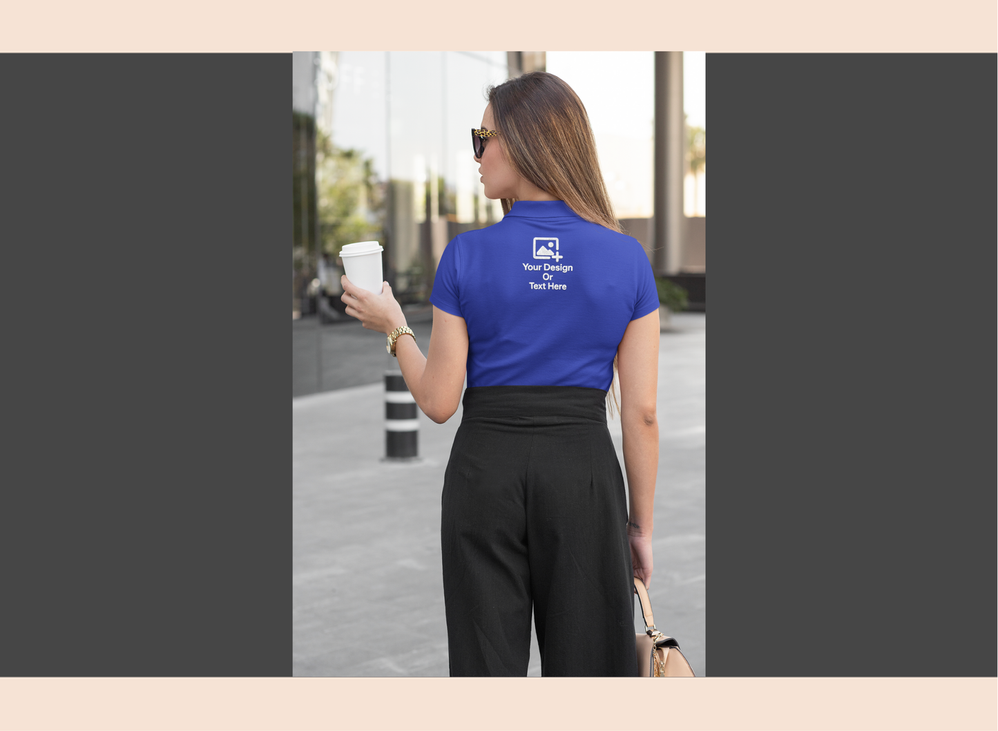 Woman wearing a blue t-shirt with a logo and text, holding a coffee cup on a city street.