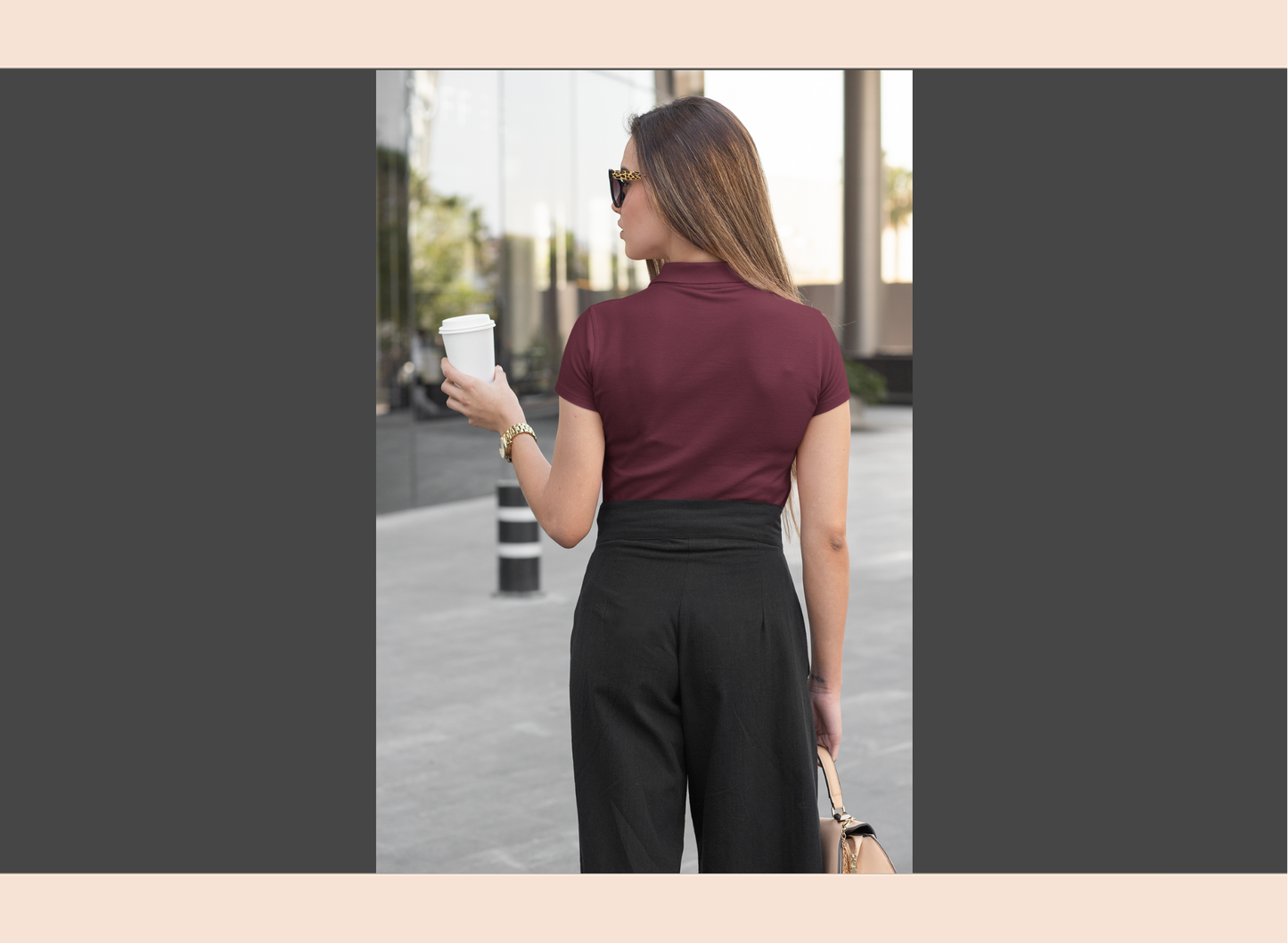 Woman in maroon shirt and black pants holding a coffee cup outdoors.