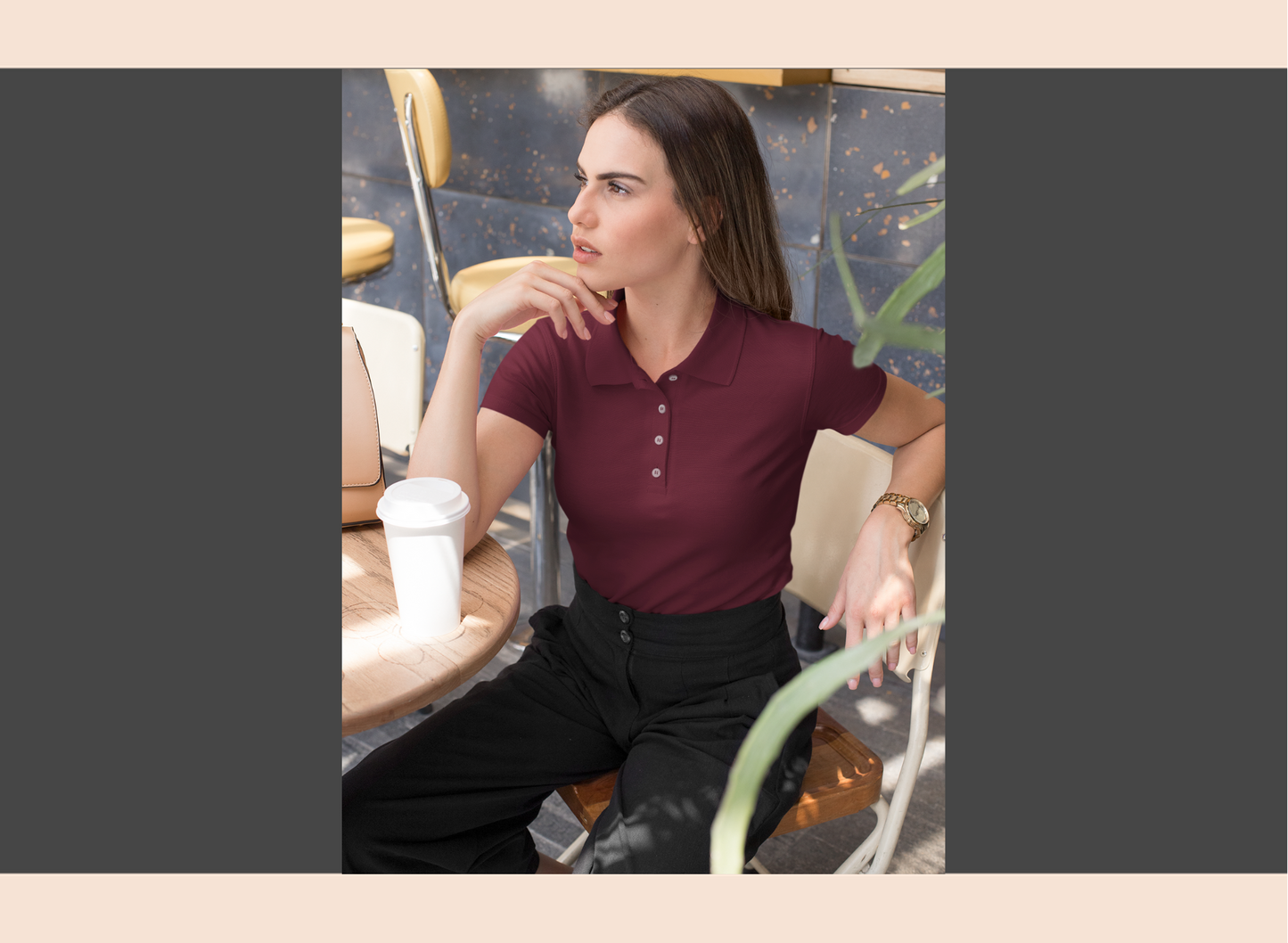 Woman sitting at a table with a drink, wearing a maroon polo shirt and black pants.