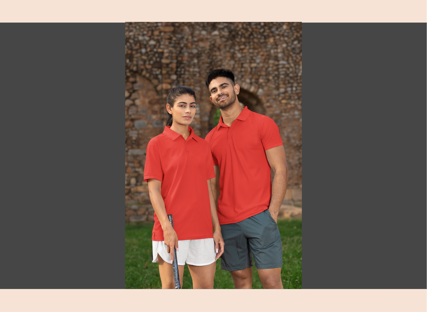 Two people wearing red polo shirts standing outdoors with a stone wall background