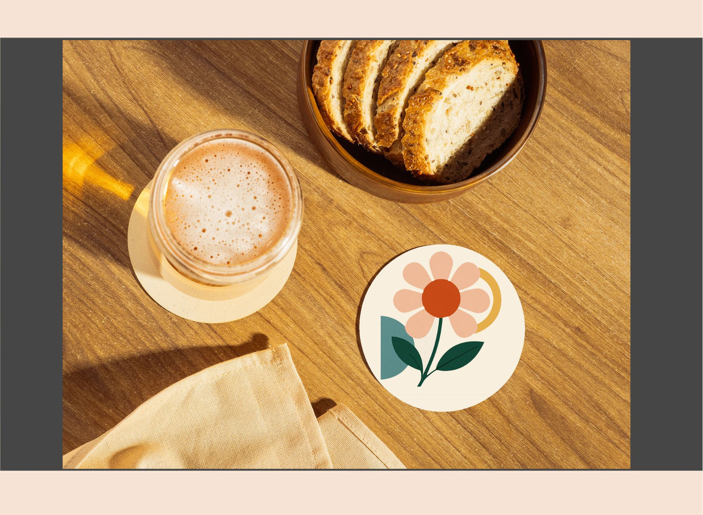 Glass of a beverage, bowl of bread, and floral coaster on a wooden surface