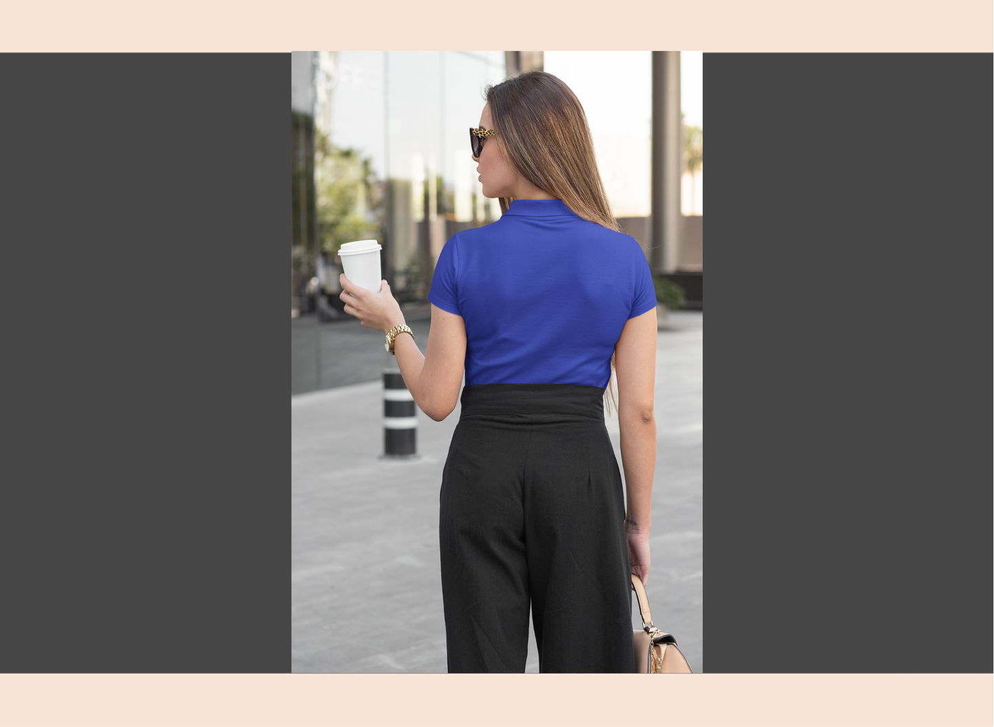 Woman in maroon shirt and black pants holding a coffee cup outdoors.