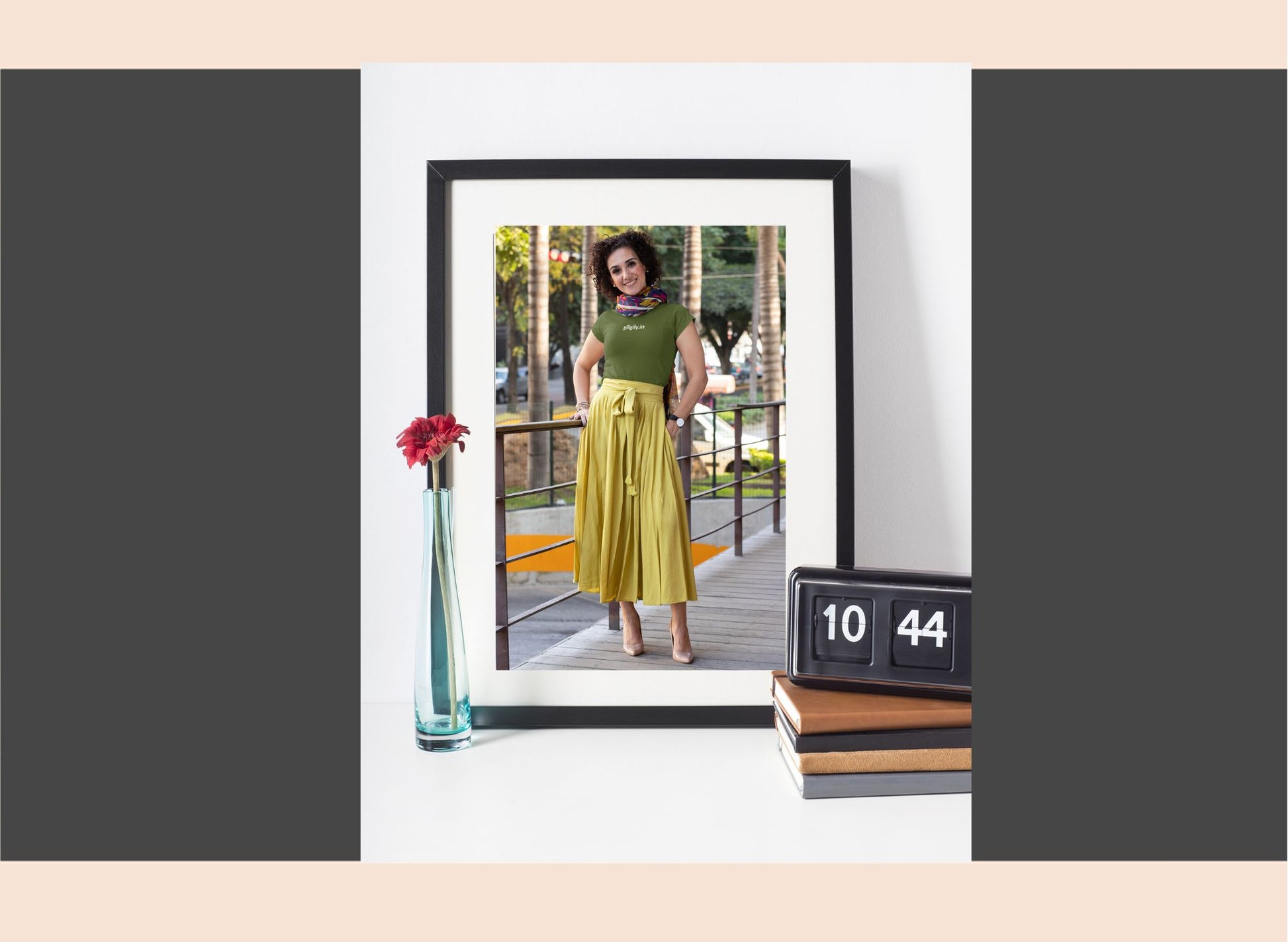 Framed photo of a woman in a green top and yellow skirt, with a vase and calendar in the foreground.