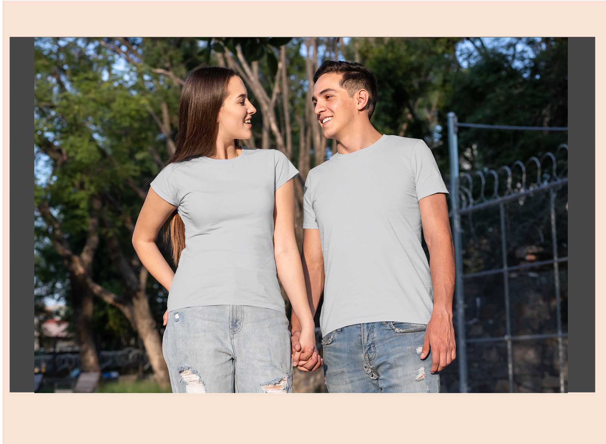 Two people standing outdoors holding hands, wearing matching gray t-shirts and jeans.