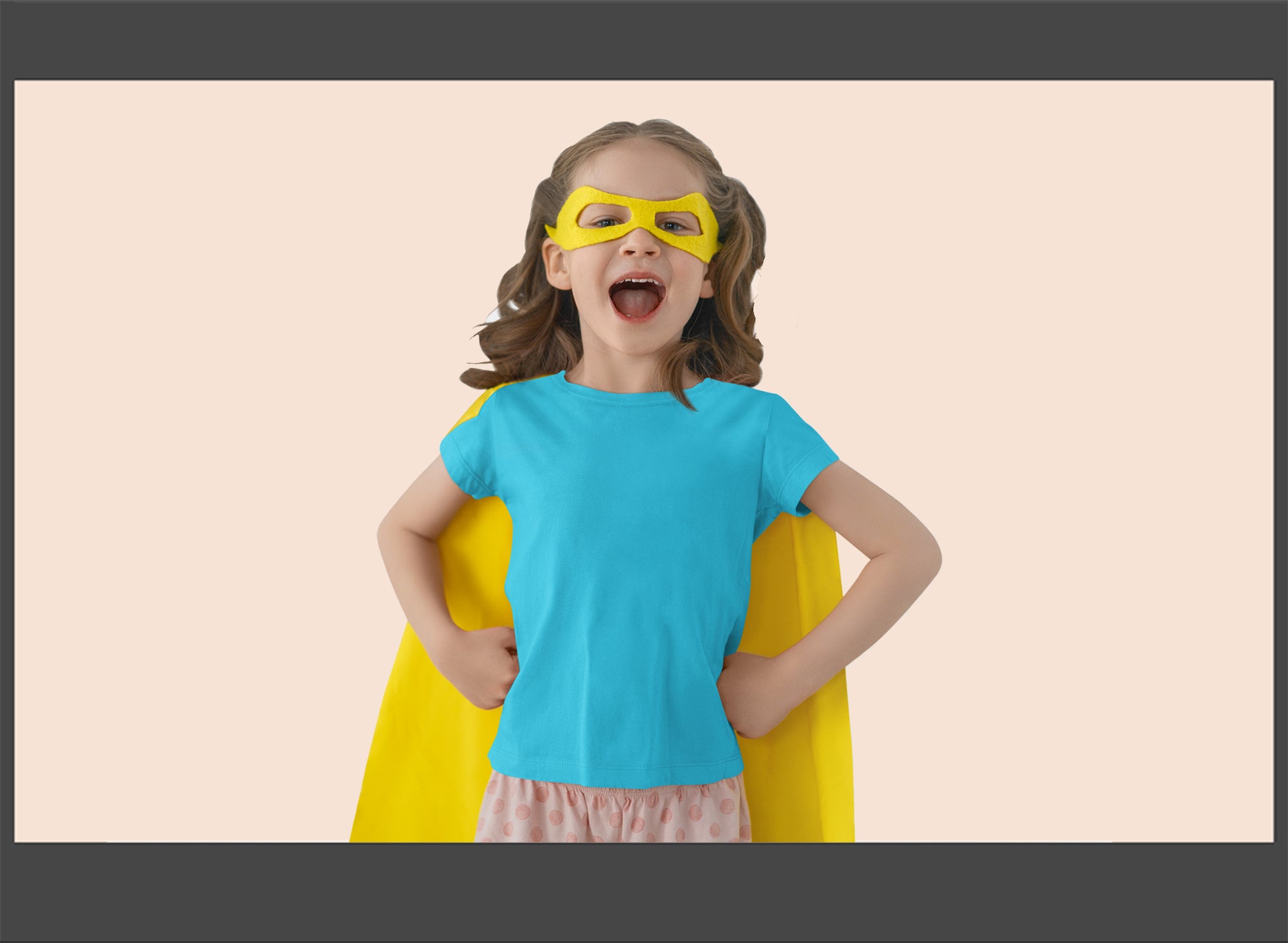 Child in superhero costume with blue shirt and yellow cape on a beige background