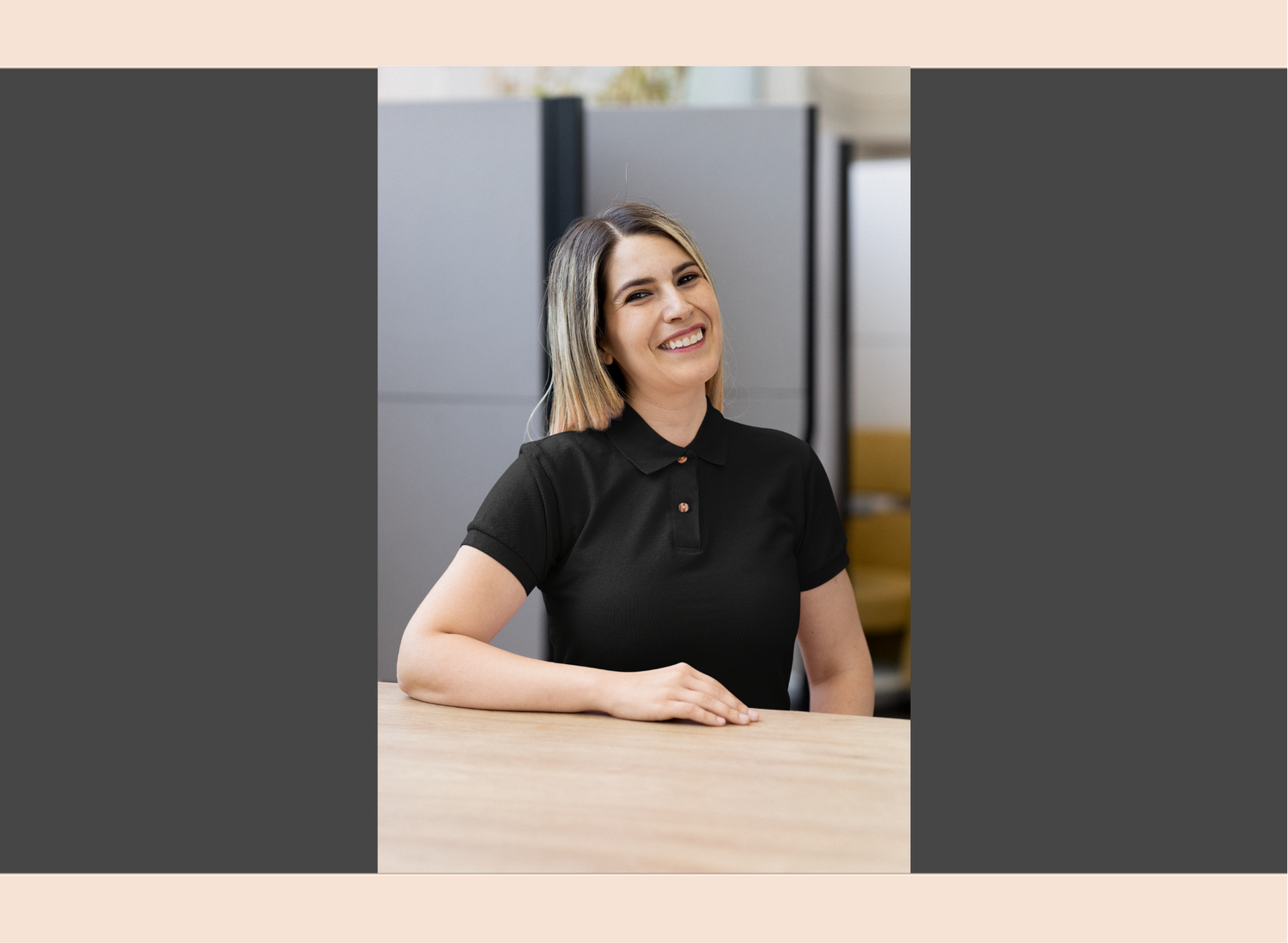 Woman in a black polo shirt sitting at a desk in an office setting