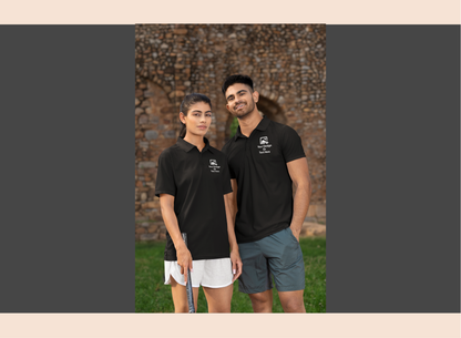 Two people wearing black polo shirts standing outdoors with a brick wall background