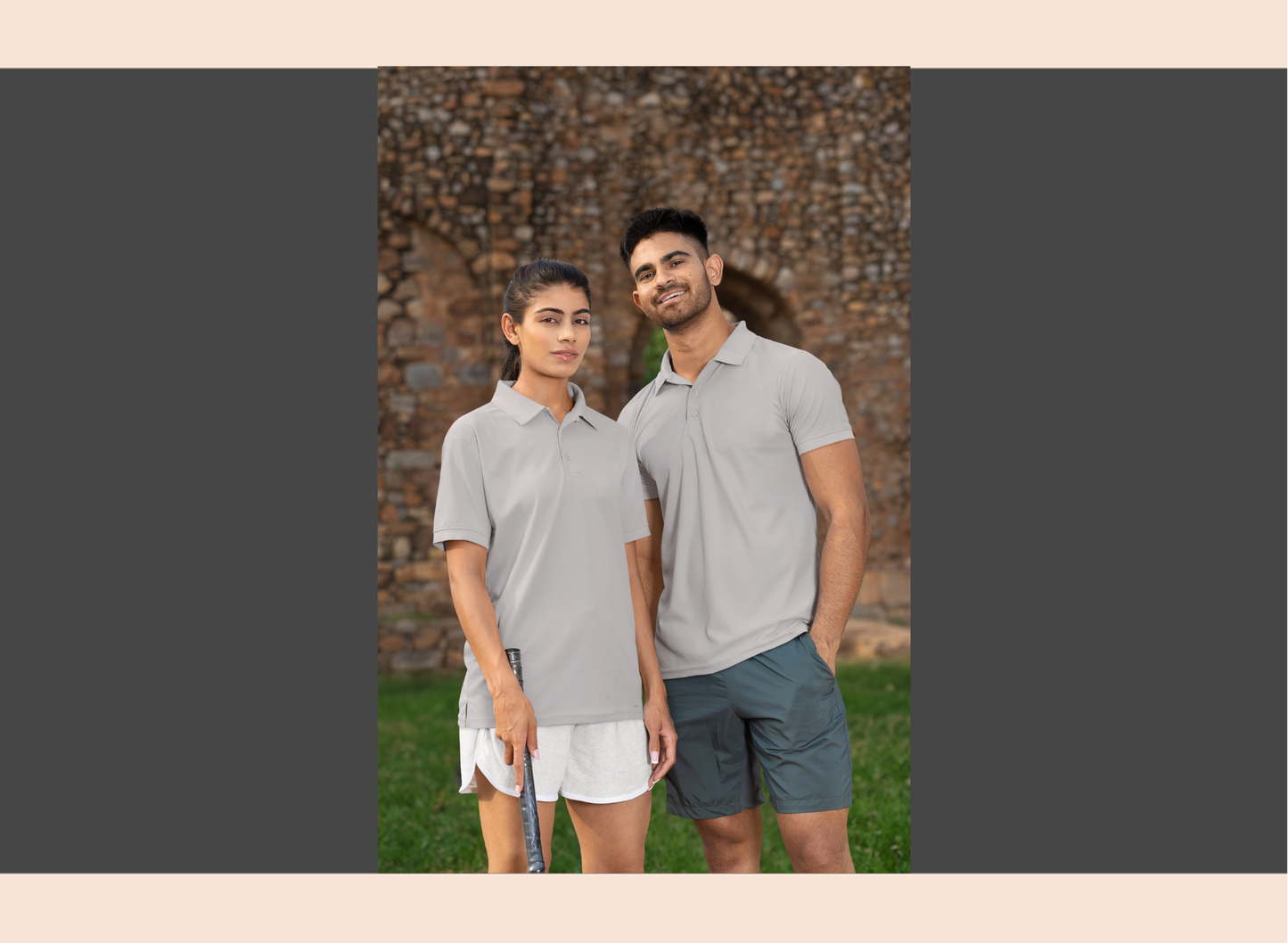 Two people wearing matching gray polo shirts and shorts standing outdoors.