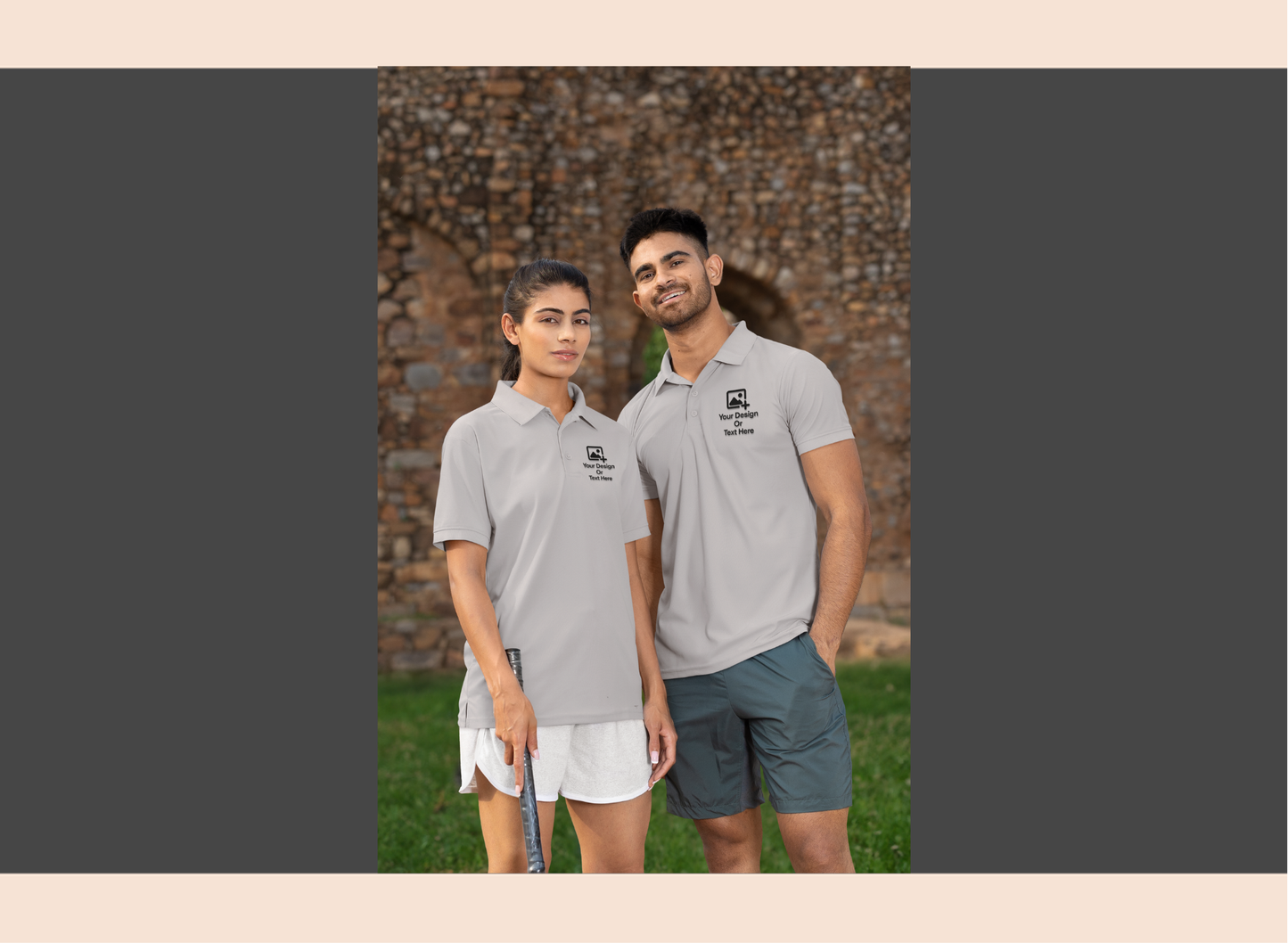 Two people wearing matching gray polo shirts standing outdoors with a stone wall background.