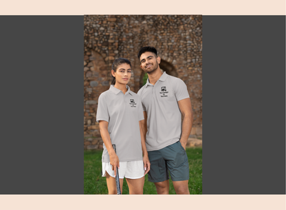 Two people wearing matching gray polo shirts standing outdoors with a stone wall background.