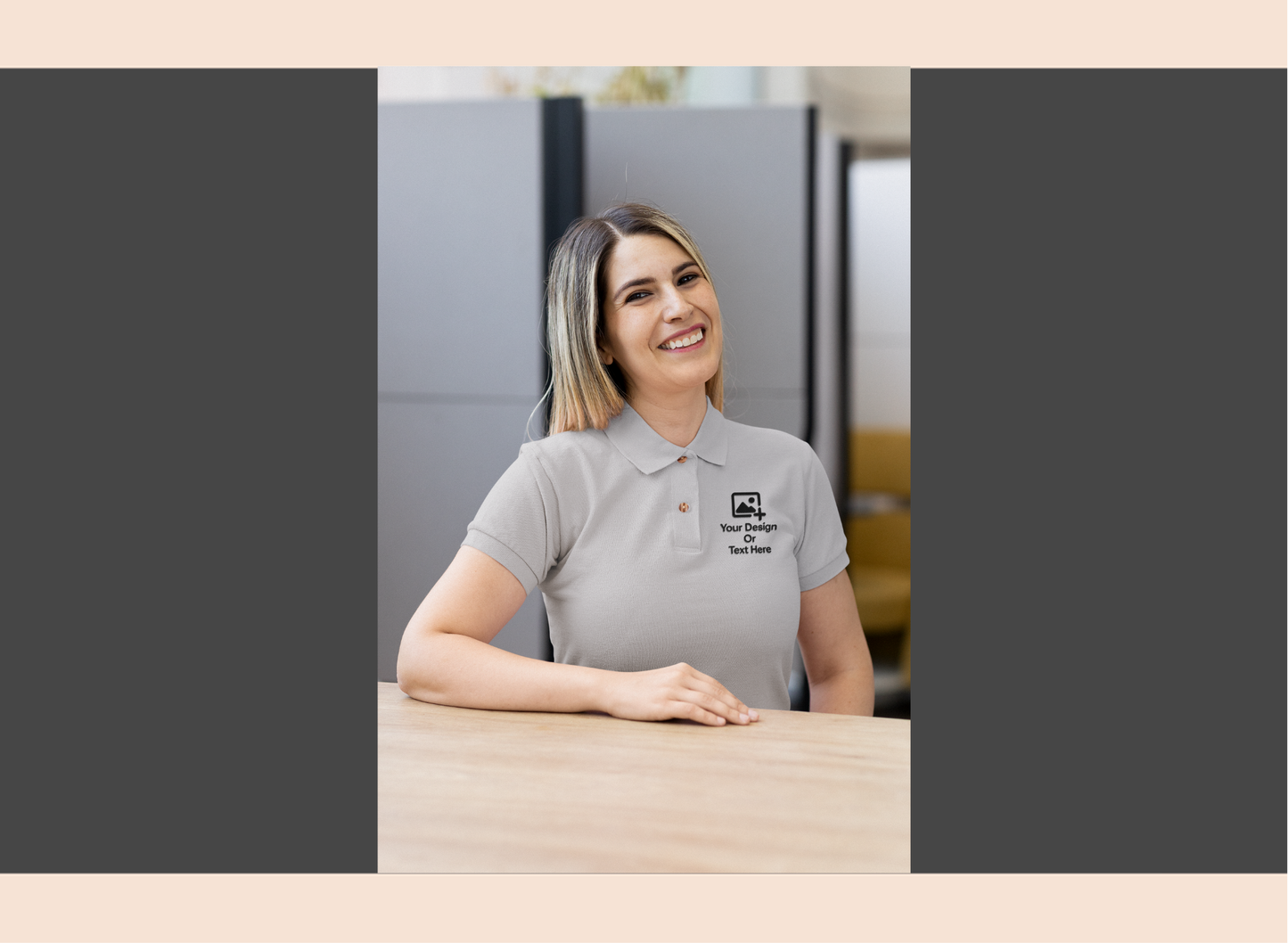 Woman wearing a gray polo shirt with a logo, sitting at a desk in an office setting.