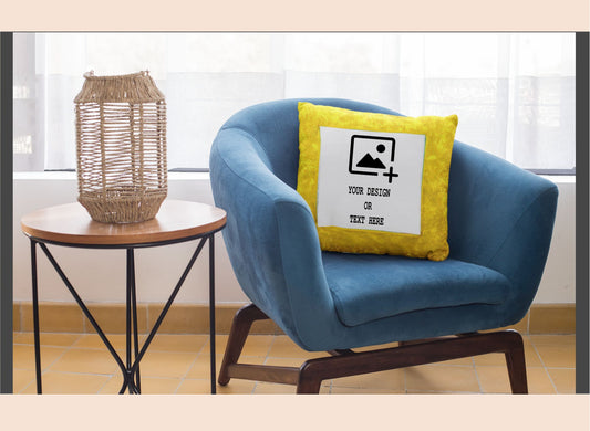 Blue armchair with a yellow pillow featuring a customizable design area, next to a small round table with a woven basket.