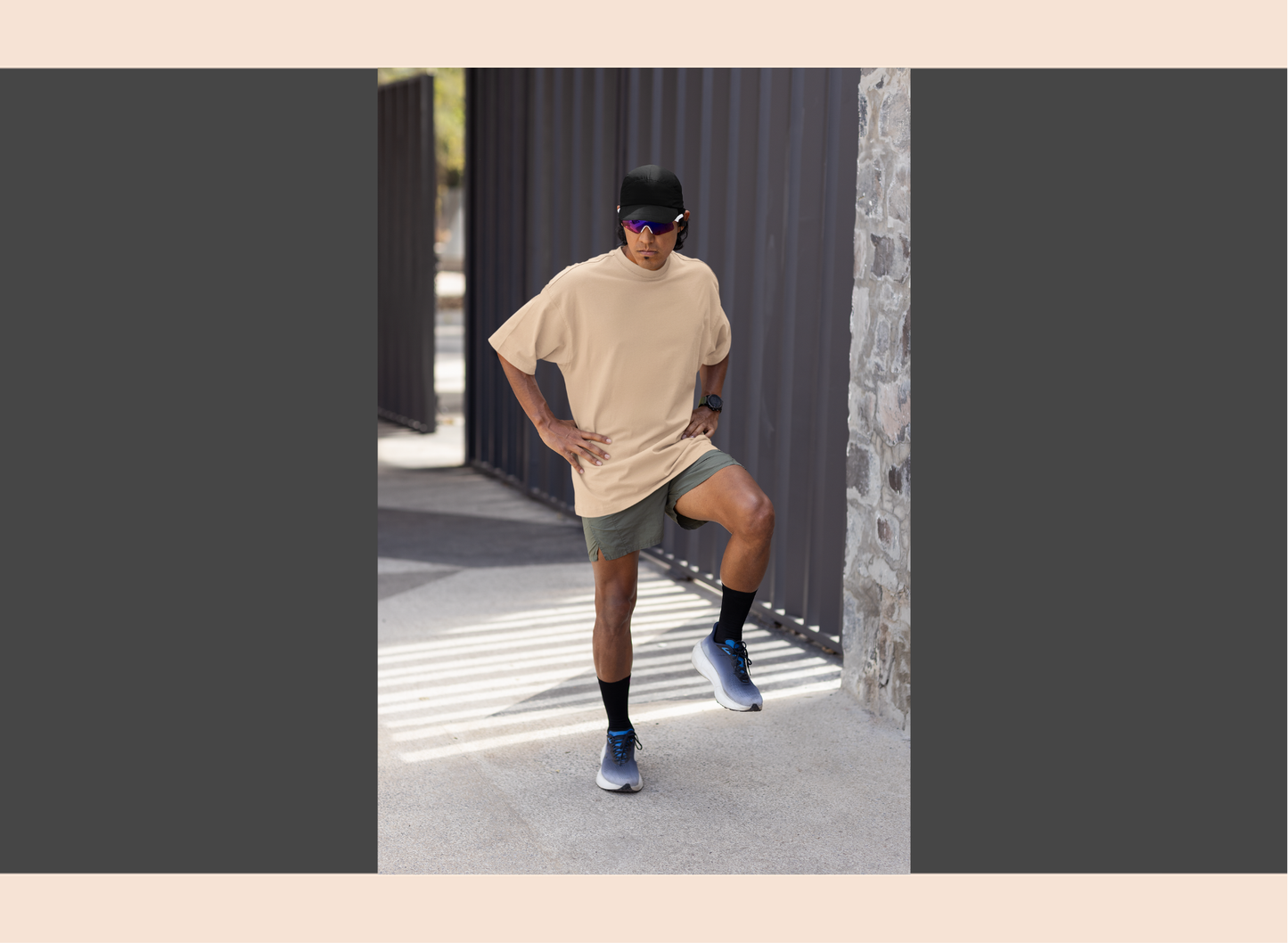 Person wearing a beige t-shirt and gray shorts standing outdoors near a stone wall.