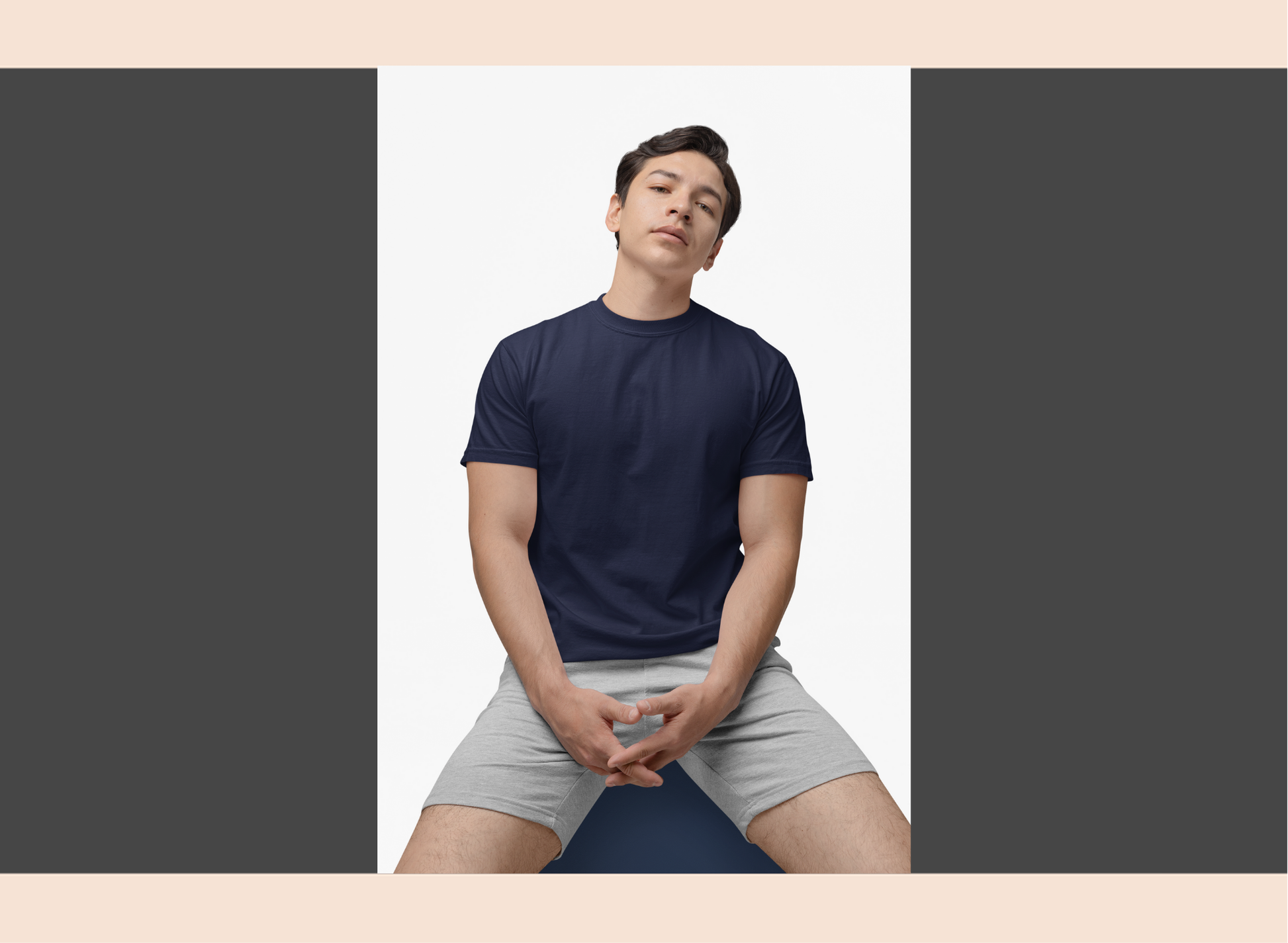 Person wearing a navy t-shirt and gray shorts sitting on a yoga mat against a plain background