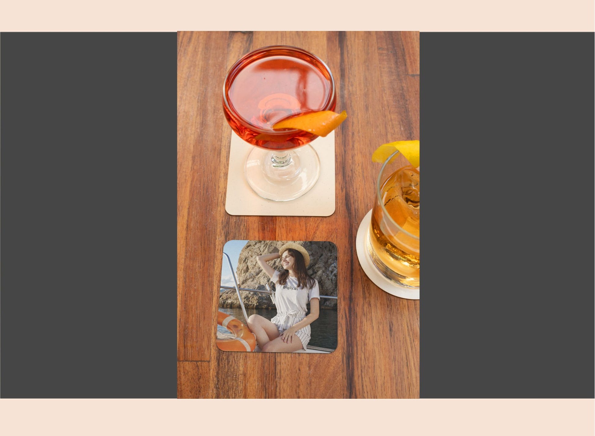 Two glasses of cocktails on a wooden table with a coaster featuring a photo of a woman.