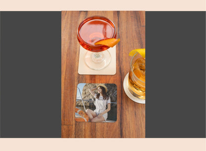 Two glasses of cocktails on a wooden table with a coaster featuring a photo of a woman.