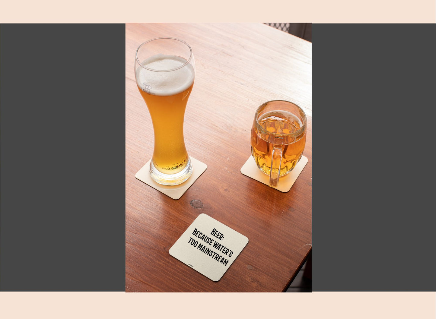 Two glasses of beer on a wooden table with a coaster underneath.
