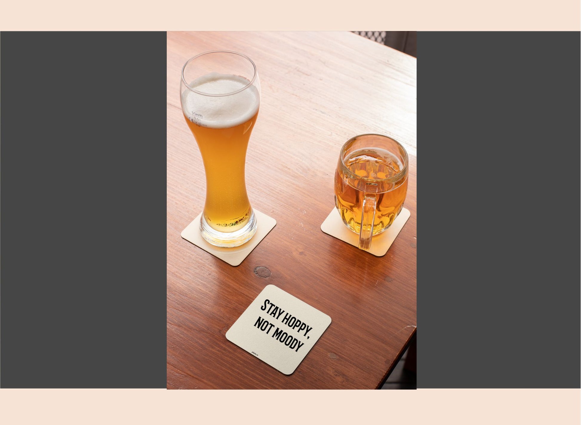 Two glasses of beer on a wooden table with a coaster underneath.
