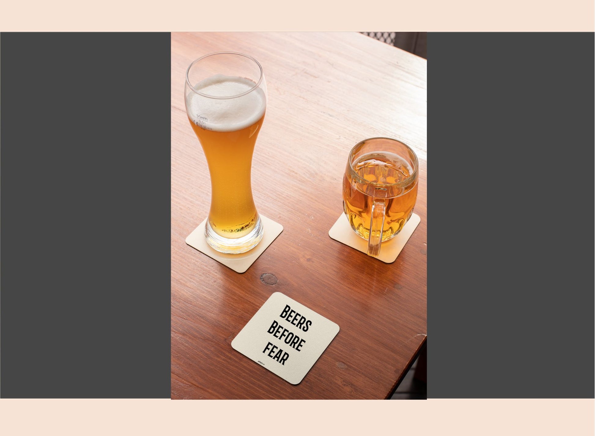 Two glasses of beer on a wooden table with a coaster reading 'BEERS BEFORE FEAR'.