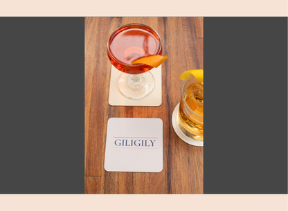 Two cocktails on a wooden table with 'GILIGILY' coasters.