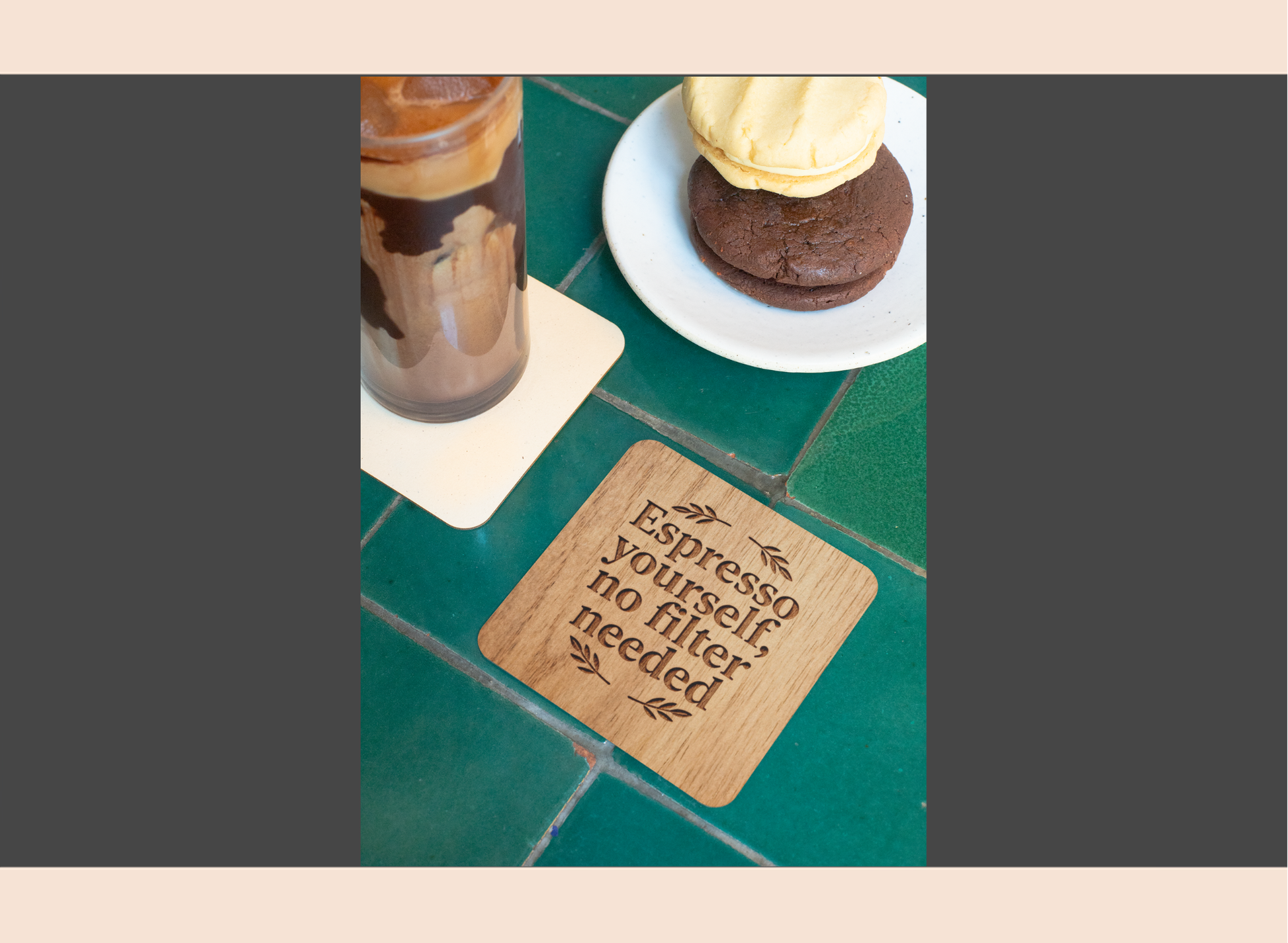 Wooden coaster with text on a green tile surface with a cup and cookies.