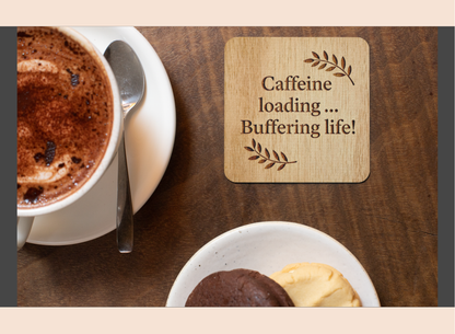 Cup of coffee with a wooden coaster reading 'Caffeine loading... Buffering life!' on a wooden table.