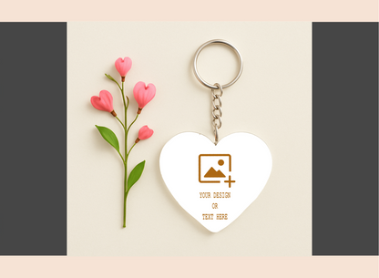 Heart-shaped keychain with customizable design area next to pink flowers on a beige background