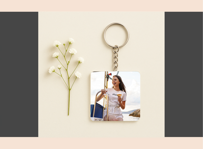 Keychain with a printed photo of a woman holding a glass of wine, placed on a light surface with a flower.